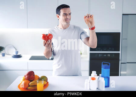 Cheerful man looking at les pilules dans sa main en se tenant debout avec une tomate Banque D'Images