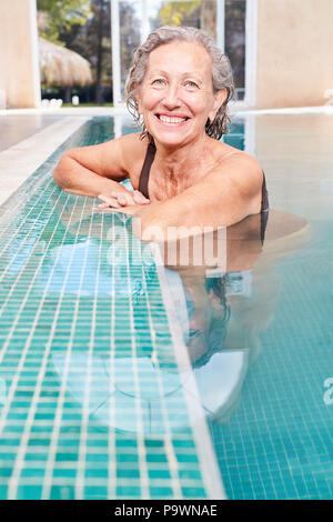 Femme heureux comme un senior woman relaxing dans la piscine au bord de la piscine Banque D'Images