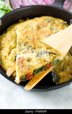 Faites de la frittata des œufs et des légumes dans une poêle de fer, sur le marbre blanc Banque D'Images