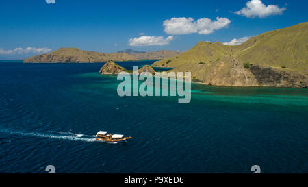 Un drone photo d'un bateau de plongée qui voyagent au-delà d'un récif, avec turquoise de l'île de Komodo et ciel bleu en arrière-plan. Komodo, Indonésie. Banque D'Images