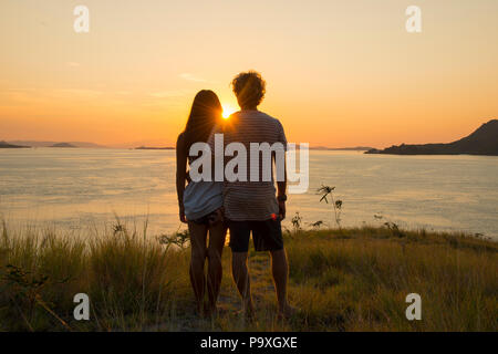 Un jeune couple de touristes debout sur un promontoire donnant sur le magnifique coucher de soleil sur le Parc National de Komodo, en Indonésie. Banque D'Images