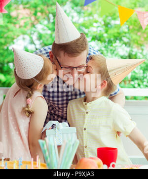 Deux enfants mignon baiser leurs jeunes et heureux père au moment de son anniversaire sur terrasse coloré décoré à la maison Banque D'Images