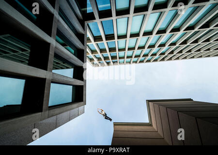 Vue de dessous du parkour masculin athlète sautant d'un toit à un autre Banque D'Images
