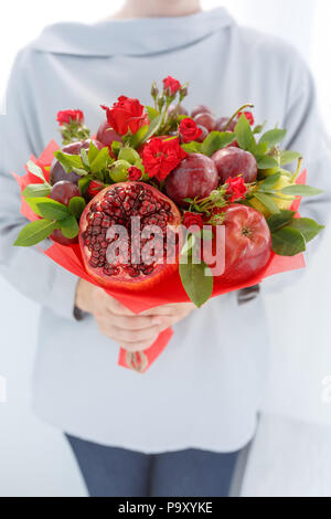 Girl détient dans les mains un bouquet de fruits original composé de pommes, prunes, poires, grenades et fleurs de roses écarlates Banque D'Images