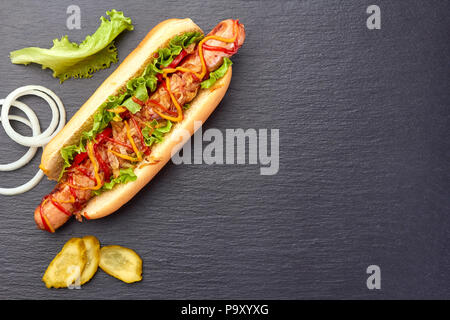 Hot dog juteux et ingrédients sur ardoise foncé Banque D'Images