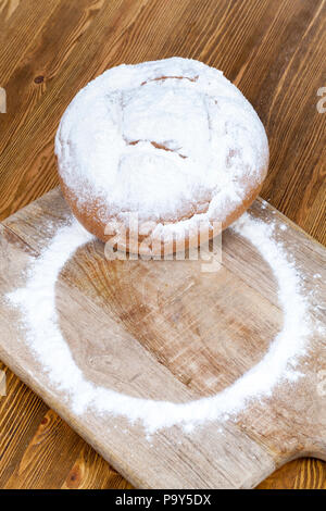 Une planche de bois et une table en bois sur laquelle se trouve une miche de pain rond saupoudrée de farine blanche, d'un close-up Banque D'Images