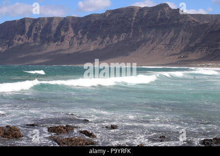 La Caleta de Famara, Lanzarote—les vagues roulent sur le rivage sous les imposantes falaises volcaniques, un spot de surf pittoresque sur la côte nord-ouest sauvage de l'île. Banque D'Images