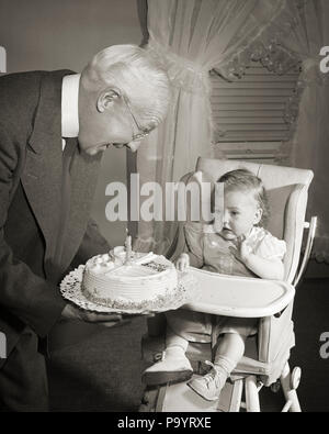 1950 Grand-père souriant présentant le gâteau d'ANNIVERSAIRE AVEC UNE BOUGIE À l'année petite-fille assis dans une chaise haute - b1321 DEB001 HARS 1 GRANDS-PARENTS GRAND-PÈRE HEUREUX JOIE JUVÉNILE CÉLÉBRATION DE VIE Les femelles d'un aîné d'un grand-parent de la vie de personnes qui s'occupent de mi-longueur HOMMES SENIOR SENIOR B&W LE BONHEUR , joyeuse excitation OLDSTERS ANTIQUES présentant la fierté aux sourires anciens petite-fille élégant JOYEUSE DEB001 juvéniles bébé fille Ensemble Noir et blanc à l'ANCIENNE Origine ethnique Caucasienne Banque D'Images