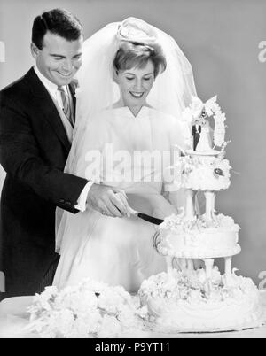 1960 GROOM HOLDING GUIDANT LA MAIN de la mariée tout en coupant le gâteau - b20892 HAR001 HARS JOIE CÉLÉBRATION DE VIE Femmes conjoint marié ÉPOUX, mi-longueur MESDAMES LES PERSONNES QUI S'OCCUPENT LES HOMMES B&W RÊVES BONHEUR aventure joyeuse excitation SOURIRES JOYEUX CONNEXION DIRECTEURS COOPÉRATION ÉLÉGANT MID-ADULT MID-ADULT MAN MID-ADULT WOMAN VÊTEMENTS DE DEUIL DEUIL SOLIDARITÉ FEMMES COSTUME NOIR ET BLANC MARIÉE ET LE MARIÉ Origine ethnique Caucasienne HAR001 old fashioned Banque D'Images