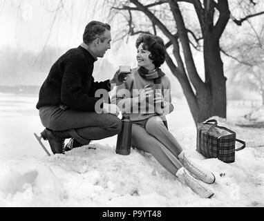 1960 SMILING COUPLE DANS LA NEIGE portant des patins à glace À PARTIR DE LA BOISSON CHAUDE POTABLE THERMOS - BW00113 CAM001 AMITIÉ HARS, mi-longueur chers hommes PERSONNES B&W datant de l'HIVER JOYEUX BONHEUR LOISIRS EXCITATION CAM001 JOYEUX SOURIRES MI-CHIC MI-HOMME ADULTE ADULTES MID-ADULT WOMAN FEMME ENSEMBLE NOIR ET BLANC à l'ANCIENNE Origine ethnique Caucasienne Banque D'Images