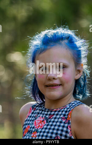 Atrtractive 8 ans, fille, dans les cheveux colorés, combinaison de saut est teint bleu lumineux, à la caméra et au comité permanent dans les arbres. Communiqué de modèle # 113 Banque D'Images