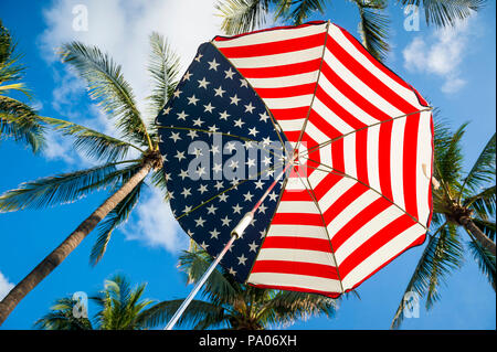 Stars and Stripes USA flag parasol ci-dessous vert tropical cocotiers et ciel tropical Banque D'Images