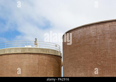 Deux grandes cuves de stockage fait de brique et de béton à une usine de traitement des eaux usées, partiellement nuageux ciel dans l'arrière-plan Banque D'Images