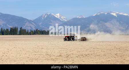 Le tracteur tirant plus de rouleaux de printemps sec dans les champs, les montagnes avec peu de neige en arrière-plan. Banque D'Images