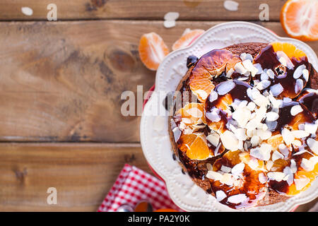 Gâteau fait maison avec les tangerines et les amandes, avec le chocolat. Sur une assiette blanche, pour le petit-déjeuner. Fond de bois, de l'espace pour écrire du texte ou de la publicité Banque D'Images