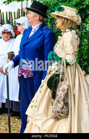 Couple, debout à l'extérieur. Habillés en costume victorien comme personnages de Charles Dickens. Il en bleu soir jaquette, elle en robe crème. Banque D'Images