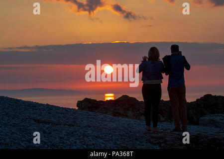 Un couple côte à côte silhouetté contre un beau coucher de soleil avec entre eux à Penmon Point, Beaumaris, Anglesey, Pays de Galles Banque D'Images