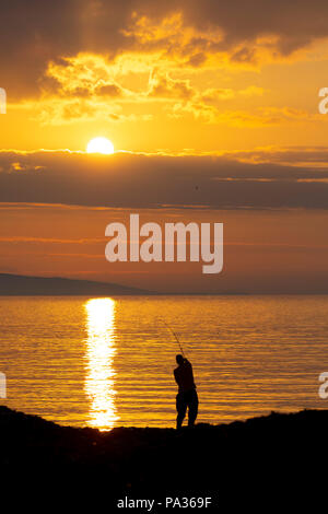 Une silhouette solitaire pêche pêcheur à Penmon Point sur Anglesey pendant un beau coucher du soleil sur la mer d'Irlande, au nord du Pays de Galles, Anglesey Banque D'Images