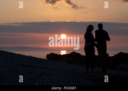 Un couple côte à côte silhouetté contre un beau coucher de soleil avec entre eux à Penmon Point, Beaumaris, Anglesey, Pays de Galles Banque D'Images