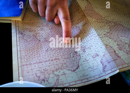 Portrait de l'homme adulte à un emplacement sur une vieille carte imprimée du monde sur une table de cuisine Banque D'Images