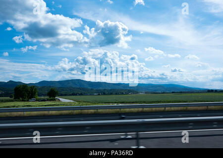 Photographie prise hors de la fenêtre de voiture sur l'autoroute de la campagne slovène avec montagnes et beaux ciel nuageux en arrière-plan Banque D'Images