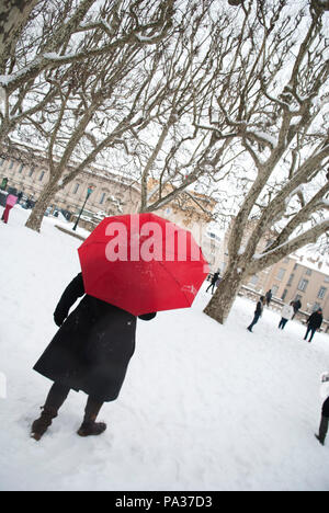 Une femme adulte sous parapluie rouge vif s'éloigner de la caméra dans un arbre rempli parc français couverte de neige et les gens en arrière-plan Banque D'Images