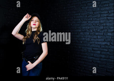 FBI agent féminin en cap et à canon au studio contre un mur de briques sombres. Banque D'Images