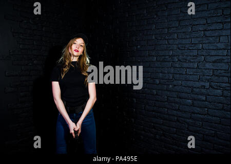 FBI agent féminin en cap et à canon au studio contre un mur de briques sombres. Banque D'Images