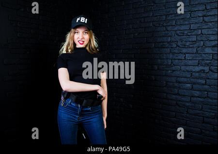 FBI agent féminin en cap et à canon au studio contre un mur de briques sombres. Banque D'Images