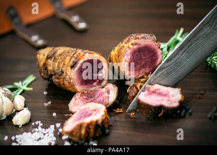 Découper une portion de rôti de bœuf biologique rouleau avec couteau sur table en bois avec de l'ail Sel et poivre à Melbourne, Australie Banque D'Images