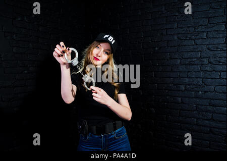 FBI agent féminin en cap et à canon au studio contre un mur de briques sombres. Banque D'Images