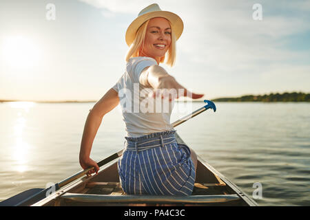 Jeune femme à l'arrière par-dessus son épaule et sa main tout en canoë sur un lac sous le soleil d'après-midi d'été Banque D'Images