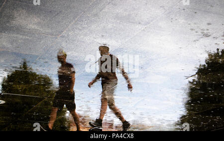 Réflexion floue silhouette de deux jeunes hommes marchant dans les rues de la ville , low angle view, dans la flaque sur un jour d'été pluvieux Banque D'Images