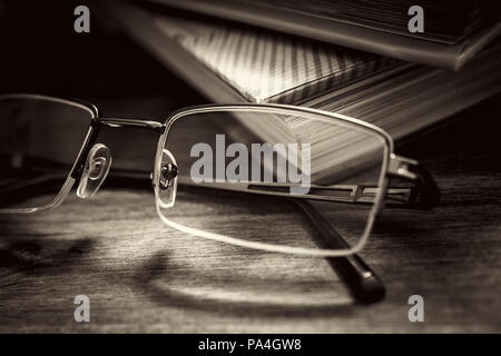 Lunettes en avant de certains livres sur table en bois dans des tons monochromes Vintage Banque D'Images