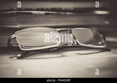 Paire de lunettes en face de certains livres sur la table de nuit en bois dans des tons monochromes Banque D'Images