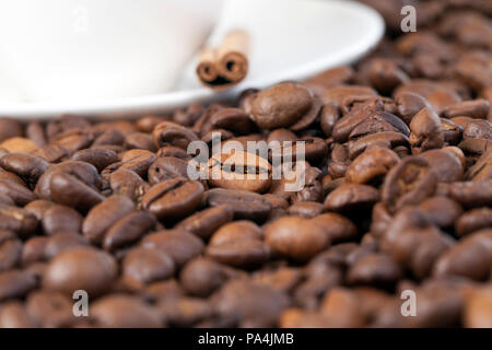Beau et parfumé poêlée de céréales entières de café, close-up, side view, dans l'arrière-plan il y a une tasse blanche sur une plaque et tout un stick de moyens Banque D'Images