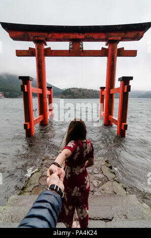 Portrait de jolies femmes tenant la main de son petit ami tout en le menant à un grand torii de Hakone Shrine construit sur le Lac Ashi. Couple dans l'amour. Banque D'Images