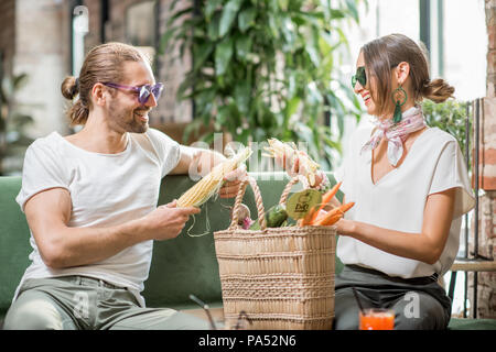 Jeune couple végétariens assis sur le canapé avec un sac plein de légumes frais dans la belle home intérieur Banque D'Images