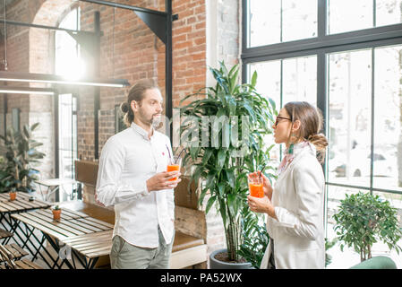 Jeune couple vêtu de blanc se tenant ensemble avec des boissons au cours de la conversation dans le magnifique intérieur loft Banque D'Images