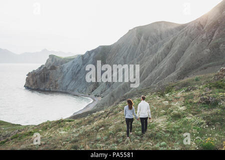 Jeune couple en train de marcher sur la côte de la mer nordique avec vue sur la montagne au printemps, les vêtements de style décontracté pulls et jeans Banque D'Images