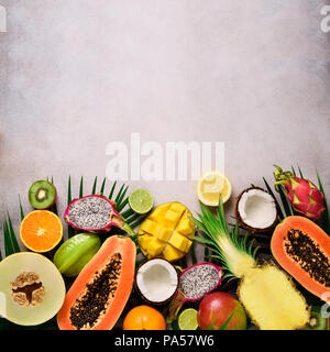 Fruits exotiques et tropicaux sur des feuilles de palmier, de béton gris - fond papaye, mangue, ananas, banane, la carambole, fruit du dragon, kiwi, citron, orange, Banque D'Images