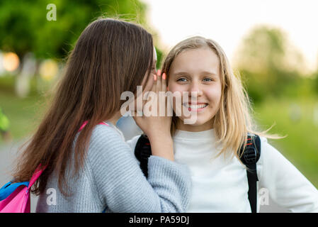 Deux jeunes filles amies d'écolière, l'été dans la ville à la nature. Il parle à l'oreille. Le concept, de mystère, de surprise, de la vérité, de don. Émotions sourire moyen Banque D'Images