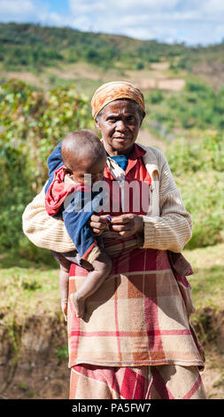 ANTANANARIVO, MADAGASCAR - 30 juin 2011 : Madagascar non identifié femme porte son enfant et d'autres choses de la rue. Les gens à Madagascar suffe Banque D'Images