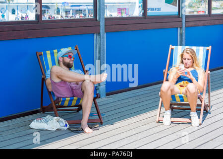 Bournemouth, Dorset, UK. 21 juillet 2018. UK : météo chaude et ensoleillée à Bournemouth plages, comme chef de la mer sunseekers pour profiter du soleil au début des vacances d'été. Dans l'ombre ou au soleil ? Couple de chaises longues sur la jetée de Bournemouth. Credit : Carolyn Jenkins/Alamy Live News Banque D'Images