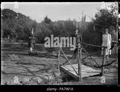 15 Albert Percy Godber debout par une passerelle sur un ruisseau étroit. Sa fille Phyllis se dresse sur la gauche, avec une tondeuse à gazon, et sa femme Laura se trouve sur la droite, dans leur jardin à Silverstream ATLIB 311700 Banque D'Images