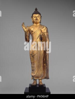 Offrant la protection de Bouddha. Culture : Sri Lanka, du plateau central. Dimensions : H. (figure) 23 3/4 in. (60,3 cm) ; W. 7 in. (17,8 cm) ; D. 4. (10,2 cm). Date : 10e siècle. Ce grand Bouddha de compassion aux fidèles des gestes de protection (Abhaya mudra) avec sa main droite posée, tandis que sa main gauche prend en charge la grande chute de sa robe monastique (uttarsanga). Les traits du visage et contour corporel suggèrent que le travail est un produit de la première période de Polonnaruva. Musée : Metropolitan Museum of Art, New York, USA. Banque D'Images