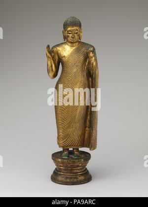 Offrant la protection de Bouddha. Culture : Sri Lanka. régions de l'ouest. Dimensions : H. 20 7/8 in. (53 cm) ; W. 5 7/8 in. (15 cm) ; Diam. du socle 5 7/16 in. (13,8 cm). Date : milieu du 15ème-16ème siècle. Cet imposant Bouddha rend l'Abhaya mudra geste avec sa main droite, en faisant preuve de compassion protection, tandis que sa main gauche prend en charge la grande chute de la robe monastique (uttarsanga). La monumentalité de l'icône est exceptionnel pour la période. Il fournit un pont stylistique entre un grand huitième siècle-fin-d'Anuradhapura style rock-cut Bouddha à Avukana et les chiffres corsé avec peignoirs dans styliz Banque D'Images