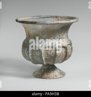 Tasse en verre avec pieds évasés. Culture : Roman. Dimensions : H. 5 3/16 in. (13,2 cm) ; diamètre 5 9/16 in. (14,1 cm). Date : 2ème moitié du 1er siècle de notre ère. Bleu translucide vert. Outsplayed jante tubulaire, repliées et dans une courbe de hauteur ; cou, effilé vers le bas ; projection d'épaule ; épais corps globulaire, squat, appliquée, Pied conique formé à partir d'un autre suppose, avec edge craquer-off et rodé ; petit, rond, fond plat. Onze côtes verticales qui se terminent en haut relief à partir d'épaule vers le bas de caisse. Rim et le corps se brisa avec un trou à côté ; partie de pied fracturé et manquant ; peu de bulles Banque D'Images