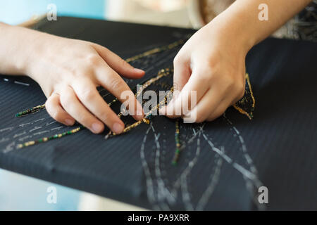 Femme avec broderie mains de fleur avec des perles. Tissu noir et les mains. Atelier Ou Design Studio sur l'adaptation. Vue en gros plan. Banque D'Images