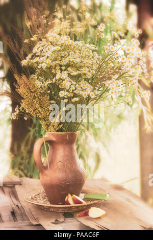 fleurs avec effet filtre style rétro vintage. Durée de vie lente. Un bouquet de chamomiles et de fleurs sauvages dans un vase en argile. Motif rural. Banque D'Images